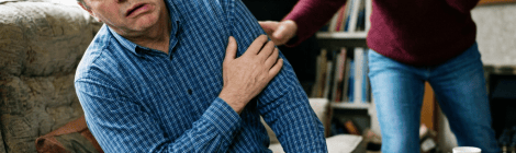 Woman calls for help as man clutches his chest in a living room